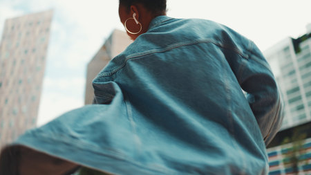 Closeup, smiling African girl with ponytail wearing denim jacket, in crop top with national pattern listening to music on headphones and dancing outdoors.の写真素材