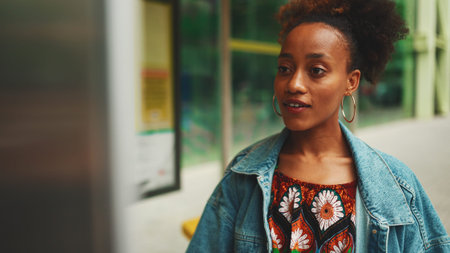 Cute African girl with ponytail, wearing denim jacket, in crop top with national pattern, standing...