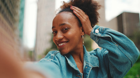 Closeup portrait of cute African girl with ponytail, wearing denim jacket makes stream, video call...