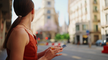 Close-up smiling young woman stands and looks at a map on a mobile phone. Girl stands on the street of the downtown scrolls the map on the smartphone.の写真素材
