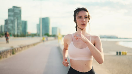 Young athletic woman with plait wearing beige sports top running sea backgroundの写真素材