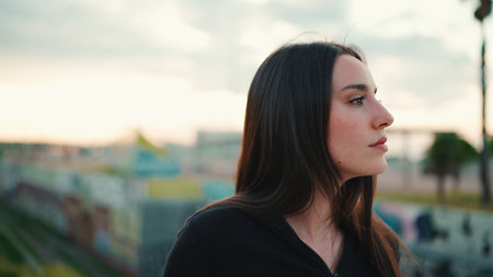 Portrait of cute girl with freckles and loose brown hair wearing black sports hoodie looks at the camera and walks on the bridge of the modern city backgroundの写真素材