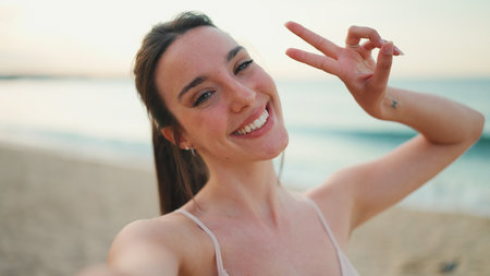 Young athletic woman with long ponytail wearing beige sports top smiling makes selfie on the sea backgroundの写真素材