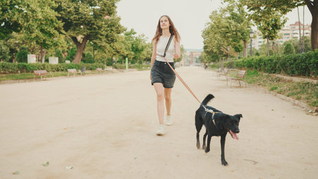 Girl walks along the path in the park with back dog.