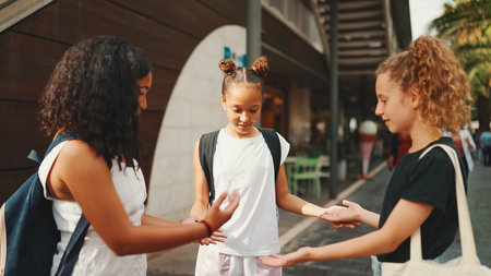 Three girls friends pre-teenage stand on the street smiling and emotionally talking, playing, clapping their hands. Three teenagers on the outdoors in urban cityscape backgroundの写真素材
