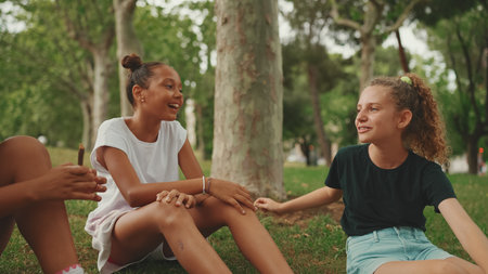 Three girls friends pre-teenage sit on the grass in the park and emotionally talking. Three teenagers on the outdoorsの写真素材