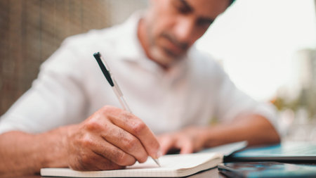 Mature businessman with beard, user on laptop pc computer and make notes sit at cafe outdoors....