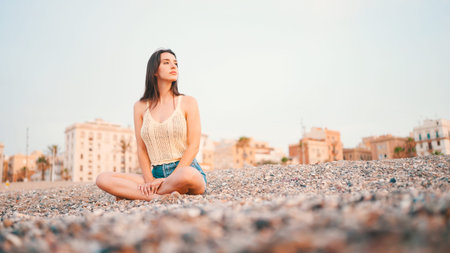 Beautiful brown-haired woman with long hair sits on the beach on seascape background. Gorgeous girl...