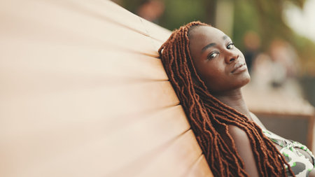 Profile gorgeous woman with African braids wearing in top and trousers is resting sitting on bench