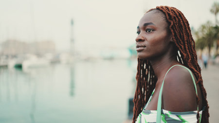 Woman with African braids wearing top looks at the yachts and ships standing on the pier in the...