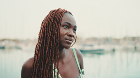 Woman with African braids wearing top looks at the yachts and ships standing on the pier in the port.の写真素材