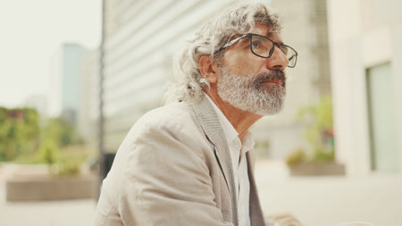 Clouse up, mature businessman with beard in eyeglasses wearing gray pondering jacket looks aroundの写真素材