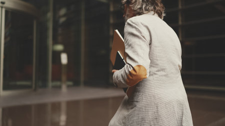 Mature businessman holding folder with business documents climbs the stairs to the business center. back viewの写真素材