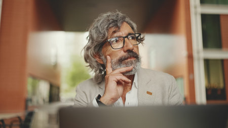 Clouse up, mature businessman with beard in eyeglasses wearing gray jacket sits on cafe. Middle aged...