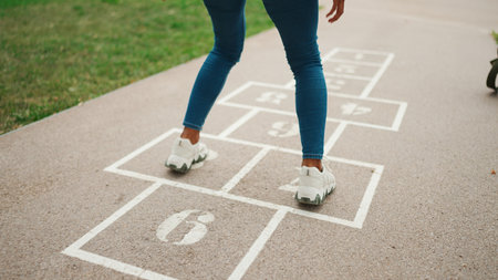 Close-up of young woman hopscotching on city playground. Closeup of the legs of girl jumping on the drawn cells on the pavementの写真素材