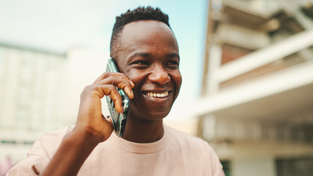 Smiling young african student sitting outside of university talking on cellphone.の写真素材