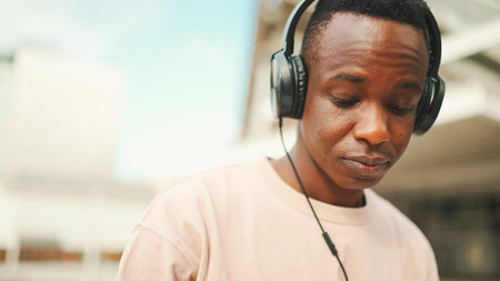 Close-up young african student sitting outside of university wearing headphones