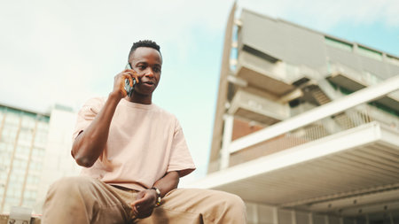 Smiling young african student sitting outside of university talking on cellphone.