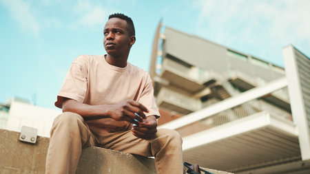 Smiling young african student sitting outside of university, looking aroundの写真素材
