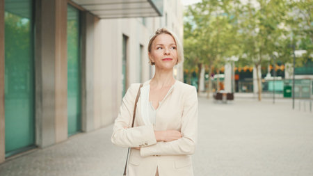 Smiling woman with blond hair wearing beige suit walks down the street and looks aroundの写真素材