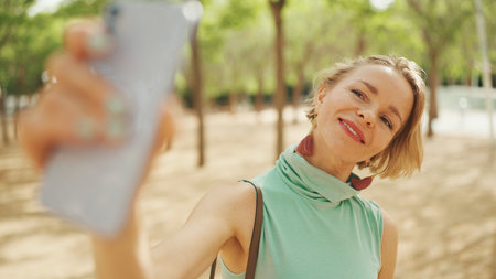 Beautiful positive woman with short blond hair in casual wear using cellphone, making video callの写真素材