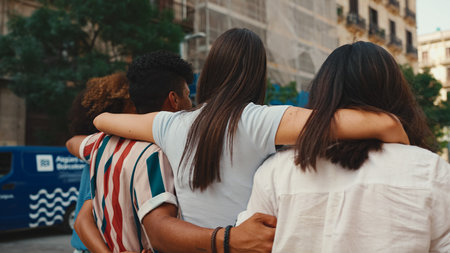 Happy multiethnic young people walk embracing on summer day outdoors. Group of friends are talking and laughing merrily while walking along on the streetの写真素材