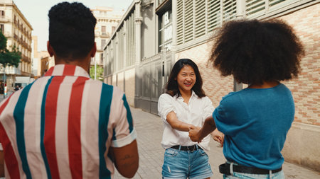 Young multiethnic women walk laughing down the street on warm summer day, meeting couple friends, enjoy meeting and huggingの写真素材