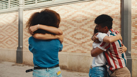 Young multiethnic women walk laughing down the street on warm summer day, meeting couple friends, enjoy meeting and huggingの写真素材