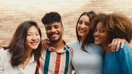 Happy, lovely multiethnic young people posing for the camera on summer day outdoors. Group of friends hugging tightly smiling at camera while standing on brick wall backgroundの写真素材