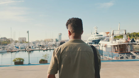 Young man dressed in an olive-colored shirt is standing in the port looking at the yachts. back viewの写真素材