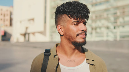 Close up, young smiling man dressed in an olive-colored shirt walks along the narrow street of the...
