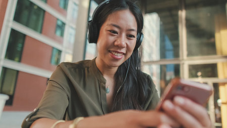 Young laughing woman freelancer in headphones works uses cellphone