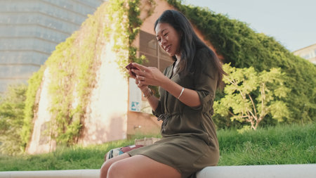Young girl uses smartphone while sitting on modern buildings backgroundの写真素材