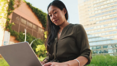 Young girl uses laptop pc outside on modern buildings backgroundの写真素材