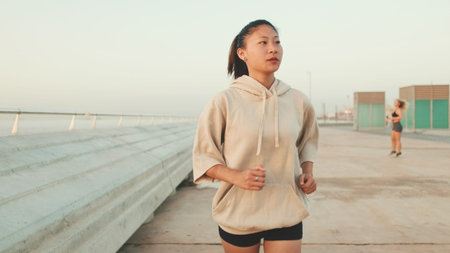 Asian young athletic woman running along the promenade. Sportswoman in sportswear exercising...