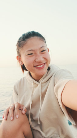 Smiling asian girl in sports top makes selfie while standing on the embankment in the morning lightの写真素材
