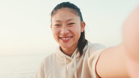 Smiling asian girl in sports top makes selfie while standing on the embankment in the morning light