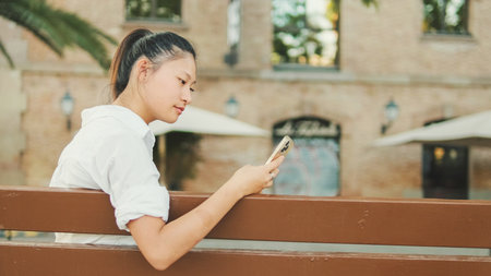 Young woman sitting on bench and using mobile phoneの写真素材