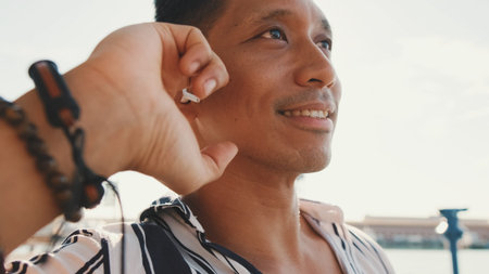 Young man tourist sits on bench on the pier talking using headset