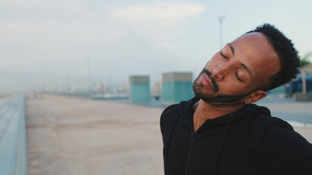 Young bearded male athlete doing warm-up before training while standing on the embankmentの写真素材