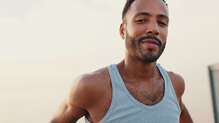 Young bearded male fit athlete standing on the embankment against the sea background, looking at the cameraの写真素材