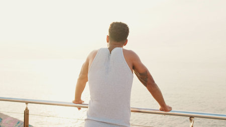 Young bearded male fit athlete standing on the embankment looking at the sea.