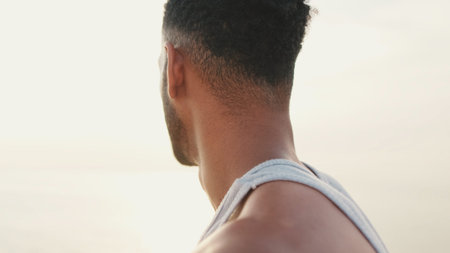 Young bearded male fit athlete standing on the embankment looking at the sea.