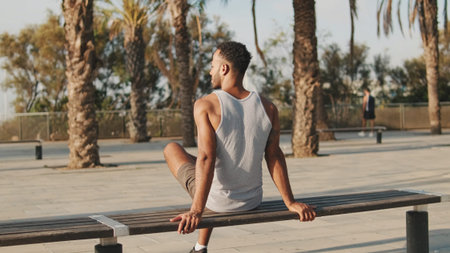 Young bearded male athlete is resting after training sitting on bench on modern background