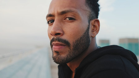 Close-up, young bearded male athlete standing on the embankment, looking at the sea. Guy turns his...