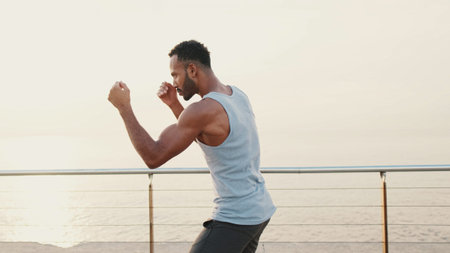 Young bearded male fit athlete boxer practicing punching technique while standing on the embankment