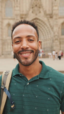Close-up of young tourist man with backpack on his shoulder, looking at the camera while standing on...