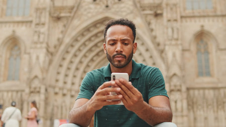 Close up, young man uses cellphone while sitting on the steps of the Sagrada Familia in Barcelona
