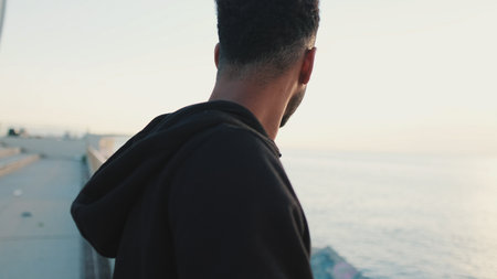 Young bearded male athlete standing on the embankment looking at the sea.の写真素材