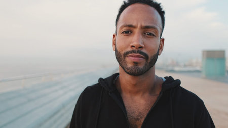 Close-up, young bearded male athlete standing on the embankment, looking at the sea. Guy turns his...